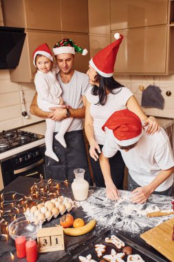 Noel şapkalı şenlik ailesi mutfakta eğlenip yemek hazırlıyor..