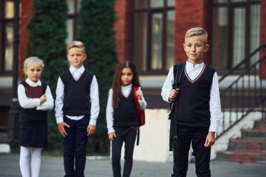 Okul üniformalı bir grup çocuk eğitim binasının yanında kameraya poz veriyor..