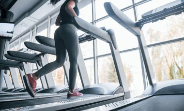 Spor elbiseli genç kız spor salonunda koşu bandında koşuyor..