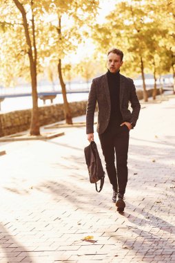 Resmi kıyafetli genç adam güneşli bir günde sonbahar parkında yürür..