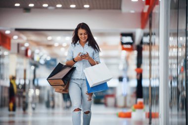 Süpermarkette elinde bir sürü paket ve telefonla esmer bir kadın alışveriş yapıyor..
