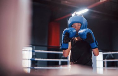 Sportif koruyucu ekipmanlı bir çocuk boks ringinde durup egzersiz yapıyor..