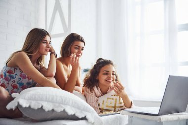 Dizüstü bilgisayarda film izlemek ve patlamış mısır yemek. Mutlu bayan arkadaşlar yatak odasında pijama partisinde iyi vakit geçiriyorlar..