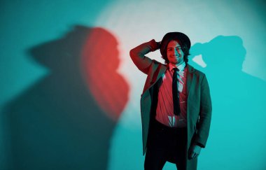 Şapkalı, takım elbiseli ve kravatlı genç bir adamın portresi stüdyodaki neon ışıklarda duruyor..