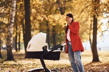 Telefonla konuşuyorum. Kırmızı ceketli anne, sonbahar zamanı çocuğuyla parkta yürüyüşe çıkar..