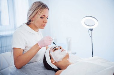 Kadın spa salonunda uzanıyor ve profesyonel kozmetik uzmanı tarafından yüz temizleme prosedürü uygulanıyor..