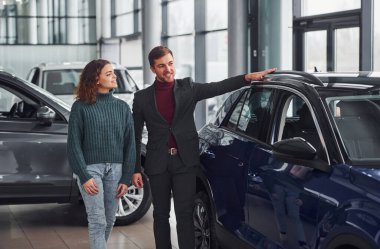 Profesyonel satıcı, genç kıza yeni modern otomobil seçerek yardımcı oluyor..