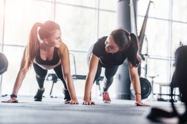 Spor elbiseli iki genç kız spor salonunda birlikte egzersiz yapıyorlar..