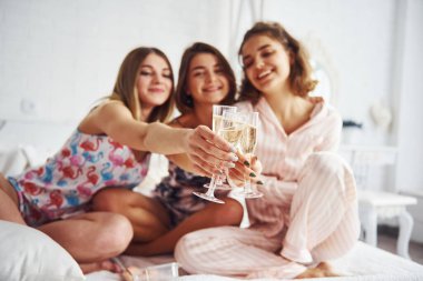 Ellerinde alkol bardaklarıyla kutluyorlar. Mutlu bayan arkadaşlar yatak odasında pijama partisinde iyi vakit geçiriyorlar..