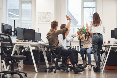 Genç iş adamları modern ofiste başarıyı kutluyorlar.