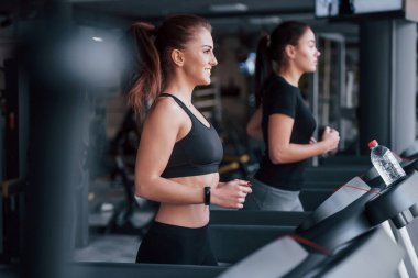 Spor elbiseli iki genç kız koşu bandında spor salonunda beraberler..
