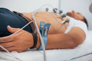 Klinikteki yatakta yatan ve elektrokardiyogram testi yaptıran bir adam..