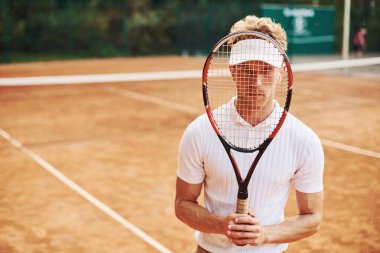 Raketi elinde tutuyor. Spor elbiseli genç tenisçi dışarıda..