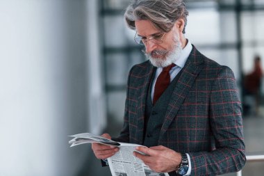 Takım elbiseli, kravatlı, gri saçlı ve sakallı kıdemli işadamı elinde gazete tutuyor..