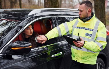 Yeşil üniformalı erkek polis memuru araçtaki kadından rüşvet almayı reddediyor..