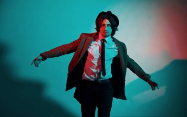 Şapkalı, takım elbiseli ve kravatlı genç bir adamın portresi stüdyodaki neon ışıklarda duruyor..