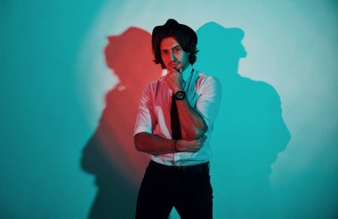 Stüdyoda neon ışıkları altında duran, resmi giyinmiş genç bir adamın portresi..