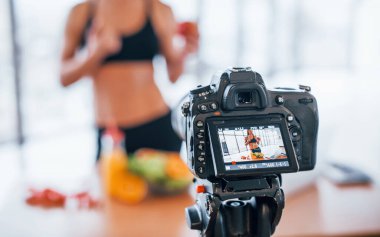 Spor vücutlu bir kadın vlogger 'ı. Sağlıklı yiyeceklerle birlikte evin içinde duruyor..