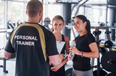 Spor elbiseli iki genç kız spor salonunda erkek özel antrenörleriyle birlikte..