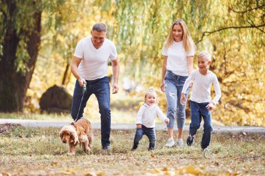 Neşeli genç aile birlikte bir sonbahar parkında yürüyüş yapıyor..