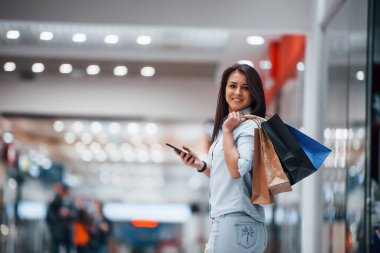 Süpermarkette elinde bir sürü paket ve telefonla esmer bir kadın alışveriş yapıyor..