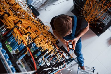 Sunucu odasında internet ekipmanı ve kablolarla çalışan ölçüm cihazıyla üniformalı genç adamın en iyi görüntüsü.