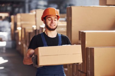 Üniformalı ve kasklı genç bir depo işçisi elinde bir kutu taşıyor..