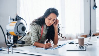 Laptop ve bir bardak içki masada. Güzel bayan işçi dikiş fabrikasında..