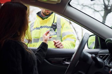 Yeşil üniformalı erkek polis yolda aracı kontrol ediyor. Rüşvet vermeye çalışan kadın.