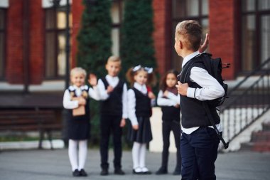 Okul üniformalı bir grup çocuk eğitim binasının yanında kameraya poz veriyor..
