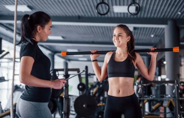 Kadın kişisel antrenör, spor salonunda egzersiz yapan kadına yardım ediyor..