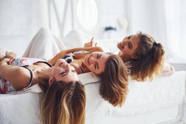 Yatağa uzanmış, saçları sarkık. Mutlu bayan arkadaşlar yatak odasında pijama partisinde iyi vakit geçiriyorlar..
