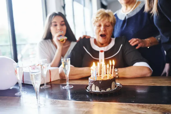 Soprar Velas Mulher Sênior Com Família Amigos Comemorando Aniversário Dentro — Fotografia de Stock