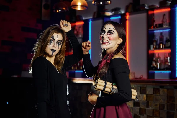 Two female friends is on the thematic halloween party in scary makeup and costumes with time bomb.