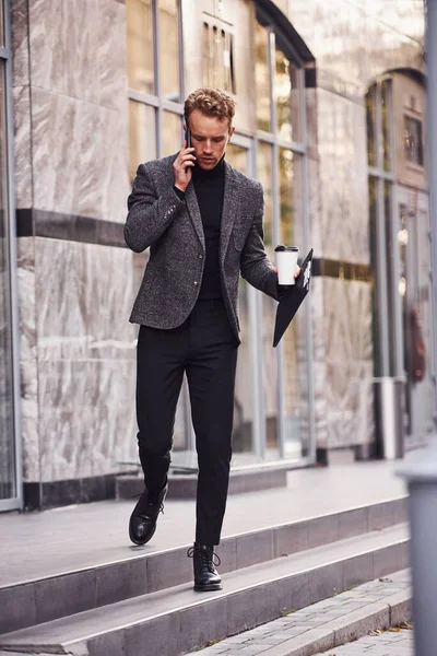Elindeki Defteri Içki Bardağıyla Şık Giyinen Adam Dışarıda Modern Binalara — Stok fotoğraf