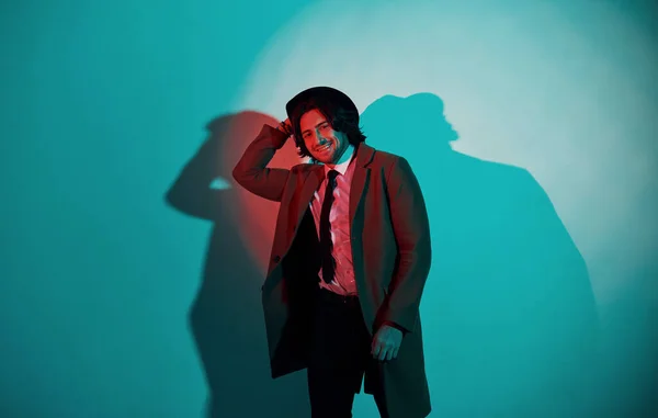 スタジオのネオンに立つ帽子 スーツ ネクタイの若いスタイリッシュな男の肖像 — ストック写真