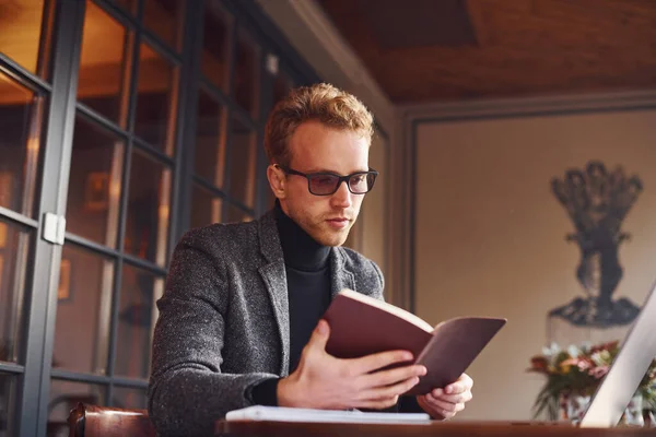 Resmi Kıyafetli Zarif Bir Genç Kafeteryada Dizüstü Bilgisayarıyla Oturur Kitabı — Stok fotoğraf