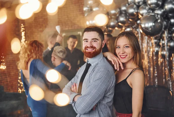 留着胡子的年轻人和他的女朋友一起站在装饰着圣诞装饰的房间里和他们的朋友们庆祝新年 — 图库照片