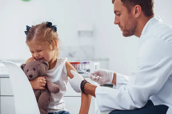 血液取样 带着玩具熊的小女孩和医生在诊所里 — 图库照片