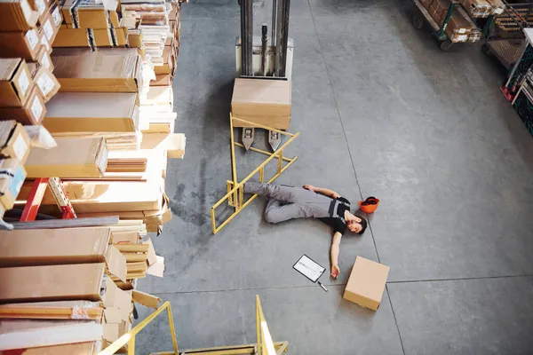 Warehouse worker after an accident in the storage. Man in uniform lying down on the ground.