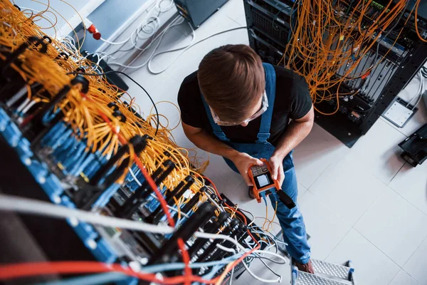 Sunucu odasında internet ekipmanı ve kablolarla çalışan ölçüm cihazıyla üniformalı genç adamın en iyi görüntüsü.