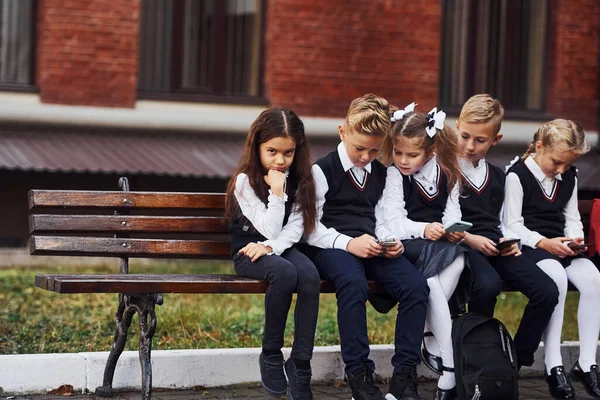 Grupo Crianças Uniforme Escolar Senta Banco Livre Juntos Perto Edifício — Fotografia de Stock