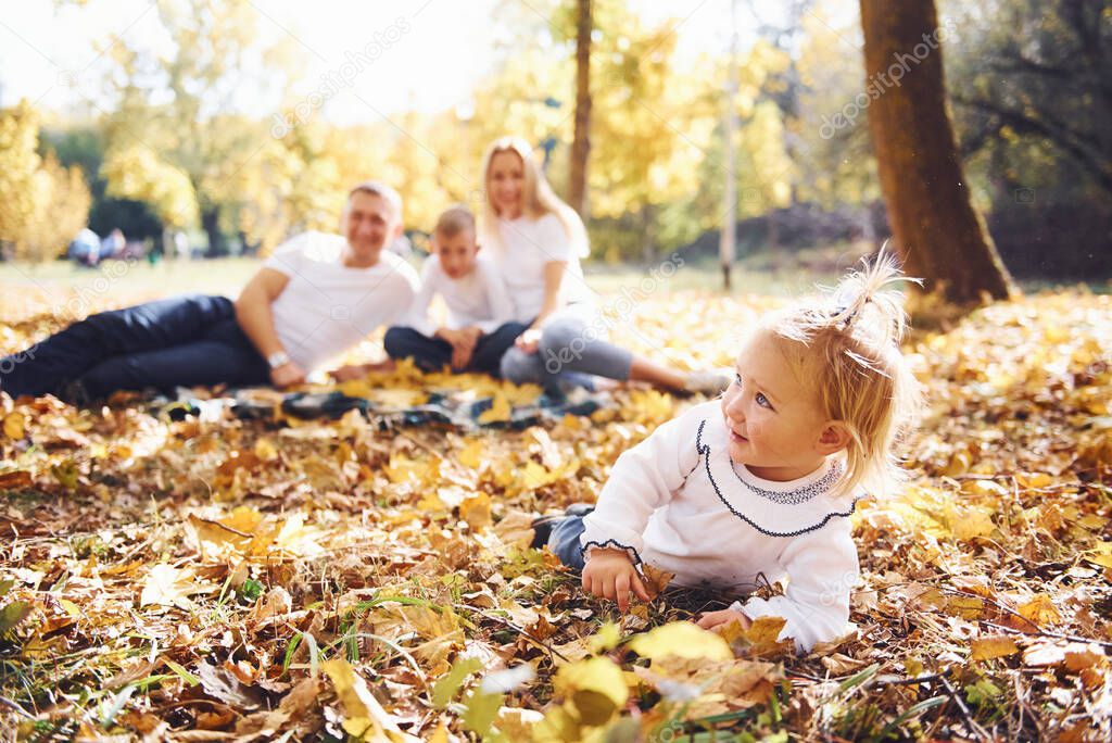 Cheerful young family lying down on the ground and have a rest in an autumn park together.