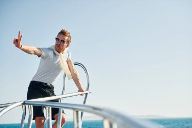 Kamera için poz vermek. Genç erkek turist denizdeki yatta. Tatil kavramı.