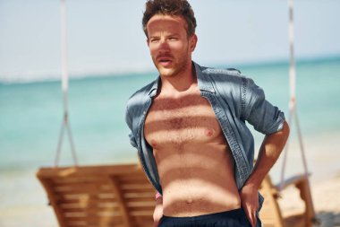 Vücudu gösteriyor. Genç Avrupalı adam tatilde ve deniz kıyısında boş zamanlarının tadını çıkarıyor..