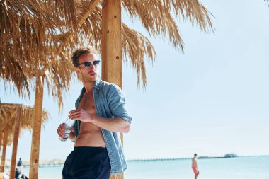 Kamera için poz vermek. Genç Avrupalı adam tatilde ve deniz kıyısında boş zamanlarının tadını çıkarıyor..