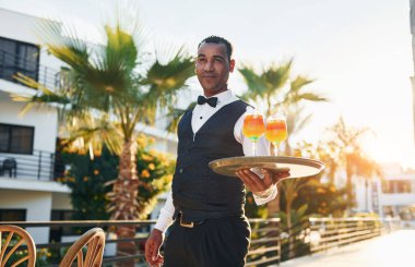 Kokteyl tutuyor. Resmi kıyafetli zenci garson güneşli bir günde iş yerinde..