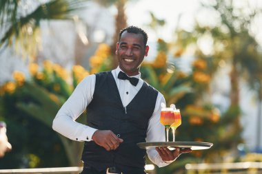 Kokteyl tutuyor. Resmi kıyafetli zenci garson güneşli bir günde iş yerinde..