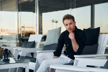 Masanın yanında oturuyor. Genç adam güneşli bir günde dışarıda. Tatil kavramı.