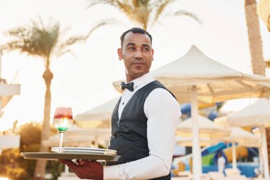 Elinde bir düzenle. Resmi kıyafetli zenci garson güneşli bir günde iş yerinde..